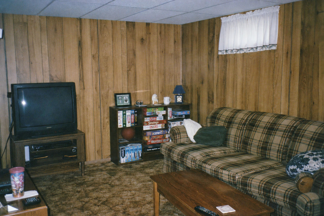 Before: a carpeted finished basement rec room with wood panelling and a low ceiling.