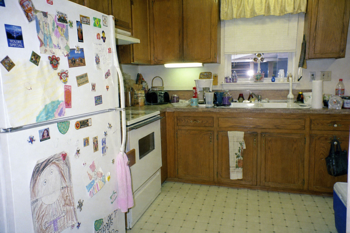 Before: a lived-in 1990s suburban kitchen with oak cabinets, linoleum floor and a cluttered counter.